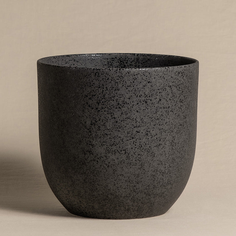 Ein minimalistischer, runder, schwarzer, heller Keramik-Topf (Direito | 22 cm ⌀) mit strukturierter Oberfläche. Der Übertopf hat eine matte Oberfläche und steht auf einer flachen Oberfläche vor einem neutralen beigen Hintergrund. Perfekt für Zimmerpflanzen, das Design ist schlicht und zeitgenössisch.