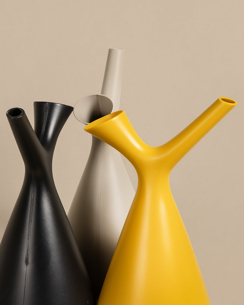 Drei moderne, minimalistische Plunge Gießkannen in Schwarz, Beige und Gelb sind vor einem neutralen Hintergrund gruppiert. Die Gießkannen haben schlanke Hälse und ein modernes Design, das sich perfekt zum Pflanzengießen eignet.
