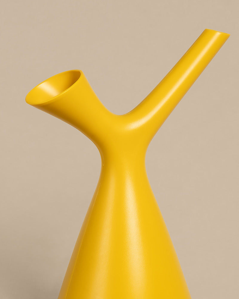 Eine elegante, moderne gelbe Plunge Gießkanne mit minimalistischem Design. Der Ausguss verläuft diagonal nach oben und hat einen schlanken Hals, ideal zum Gießen von Pflanzen. Die Öffnung ist ausgestellt und abgewinkelt und steht vor einem schlichten, neutralen beigen Hintergrund.
