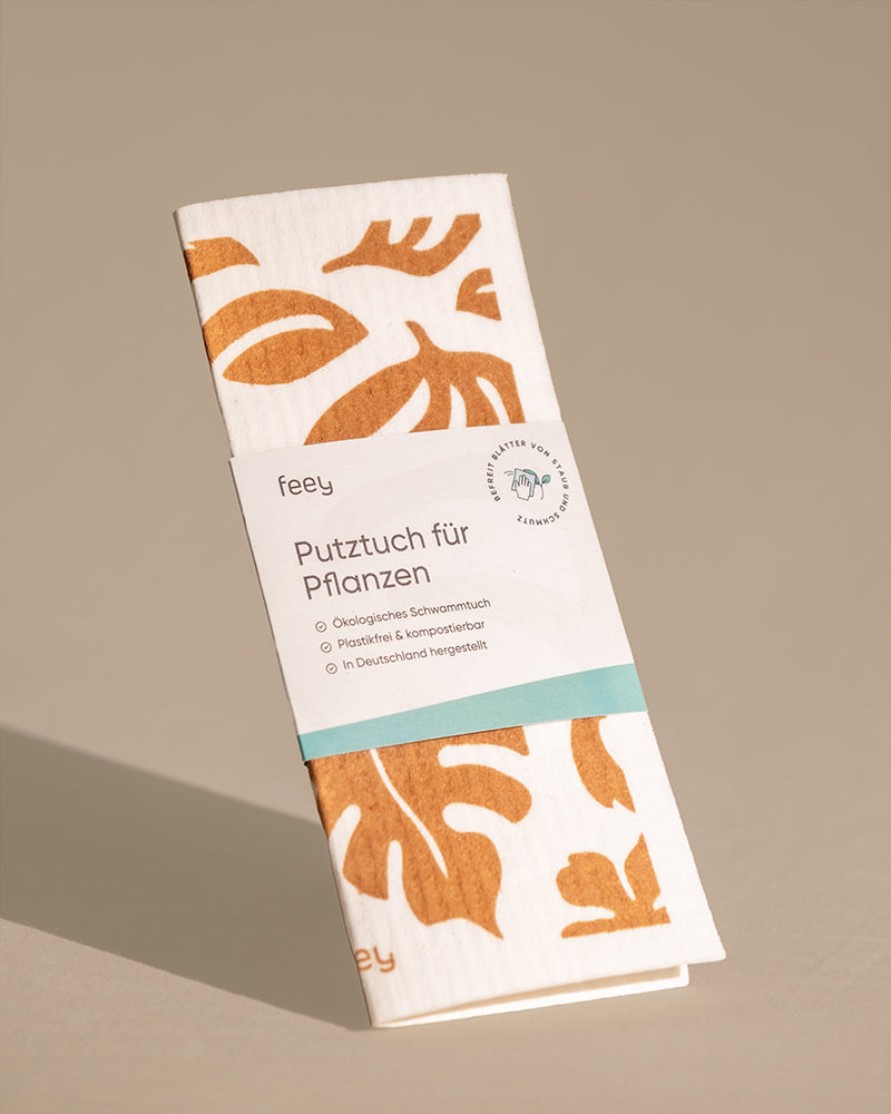 Das „Putztuch für Pflanzen“ ist ein Reinigungstuch für Pflanzen, das ein botanisches Blattmotiv in Braun auf weißem Grund zeigt. Auf der Verpackung finden Sie Informationen in deutscher Sprache, die darauf hinweisen, dass es sich um ein ökologisches Schwammtuch handelt, das in Deutschland hergestellt und kompostierbar ist. Ideal für die effiziente Pflege Ihrer Pflanzen.