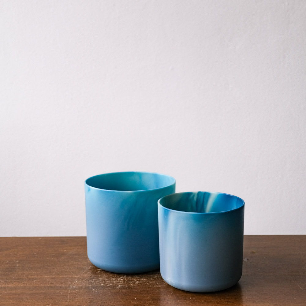 Zwei blaue Topfsets (18, 16) unterschiedlicher Größe stehen auf einer Holzfläche vor einem schlichten weißen Hintergrund. Die Töpfe weisen einen Farbverlauf von dunkleren zu helleren Blautönen auf, was für eine ruhige und beruhigende Wirkung sorgt.